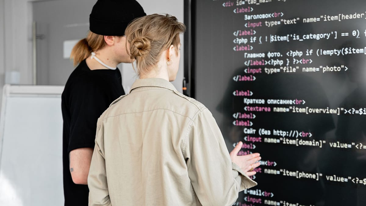 Two colleagues discussing lines of code on a large wall screen