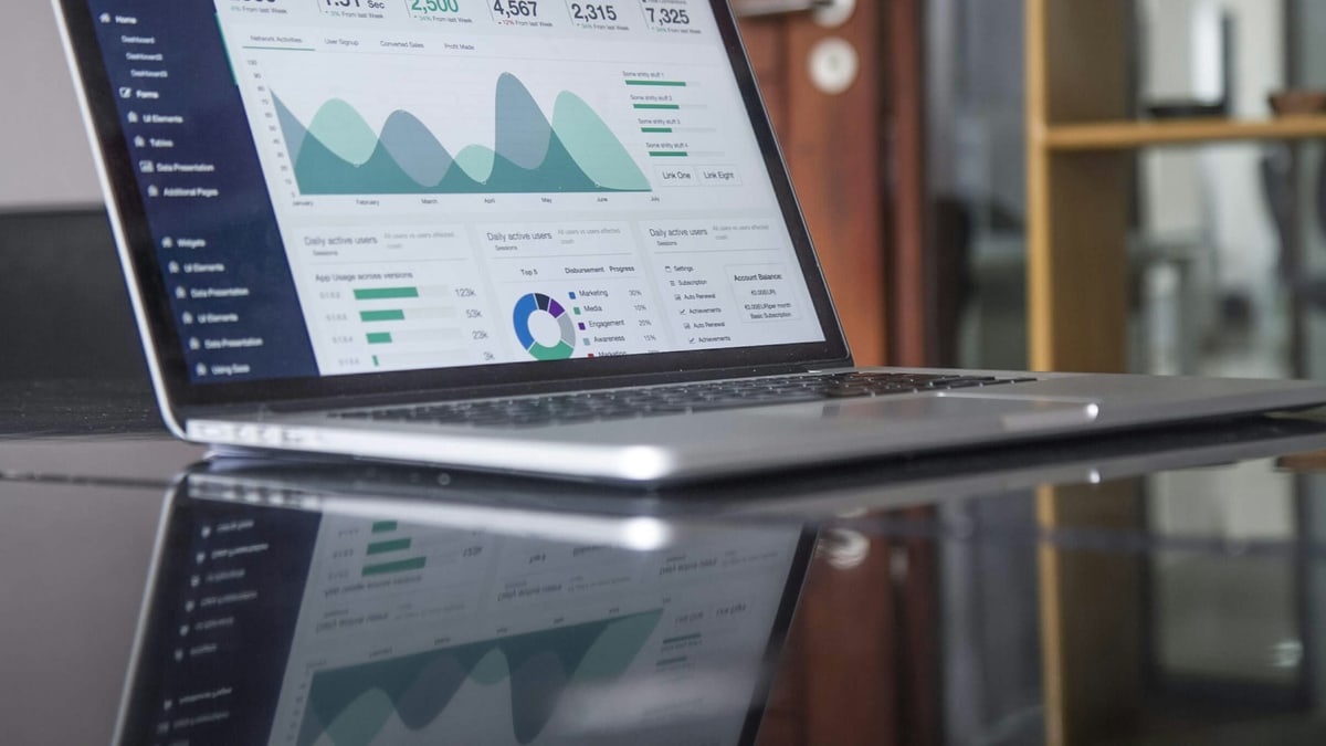 A laptop on a glass table showing an analytics dashboard with charts