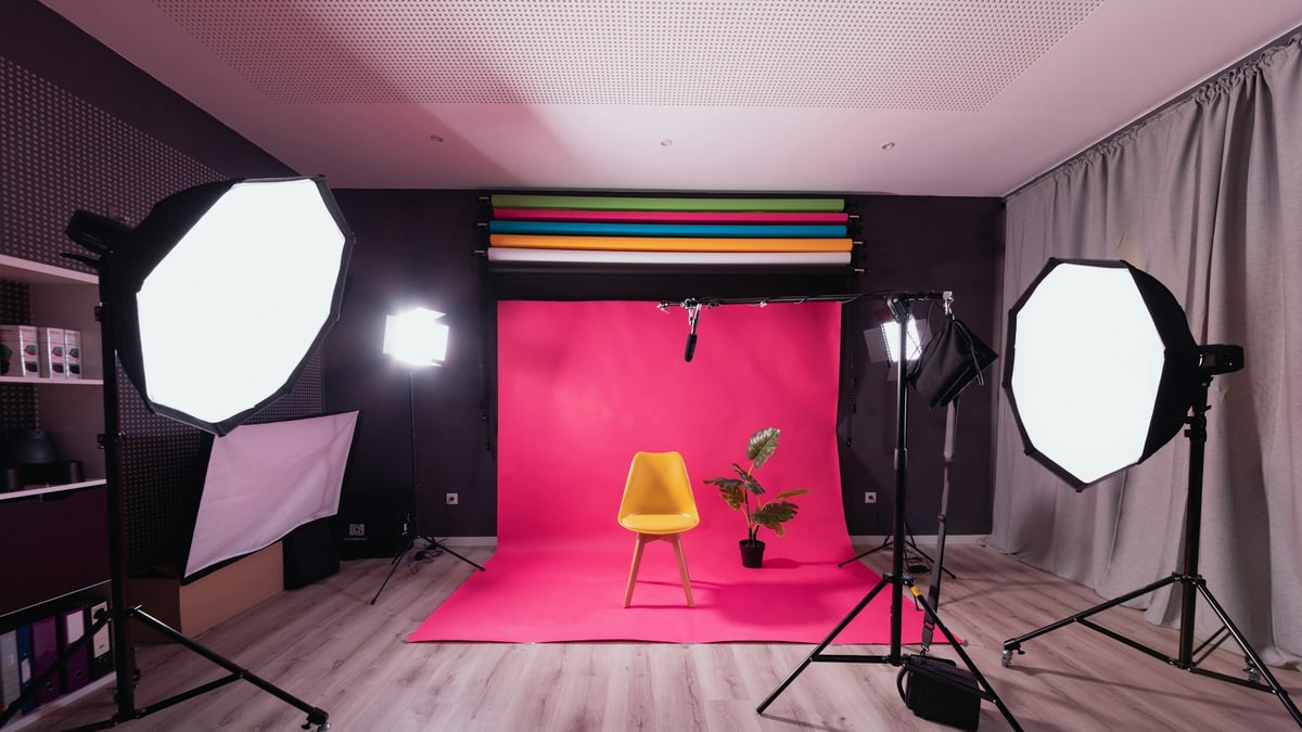 A photo studio with a pink backdrop, a yellow chair and studio lights for product shoots