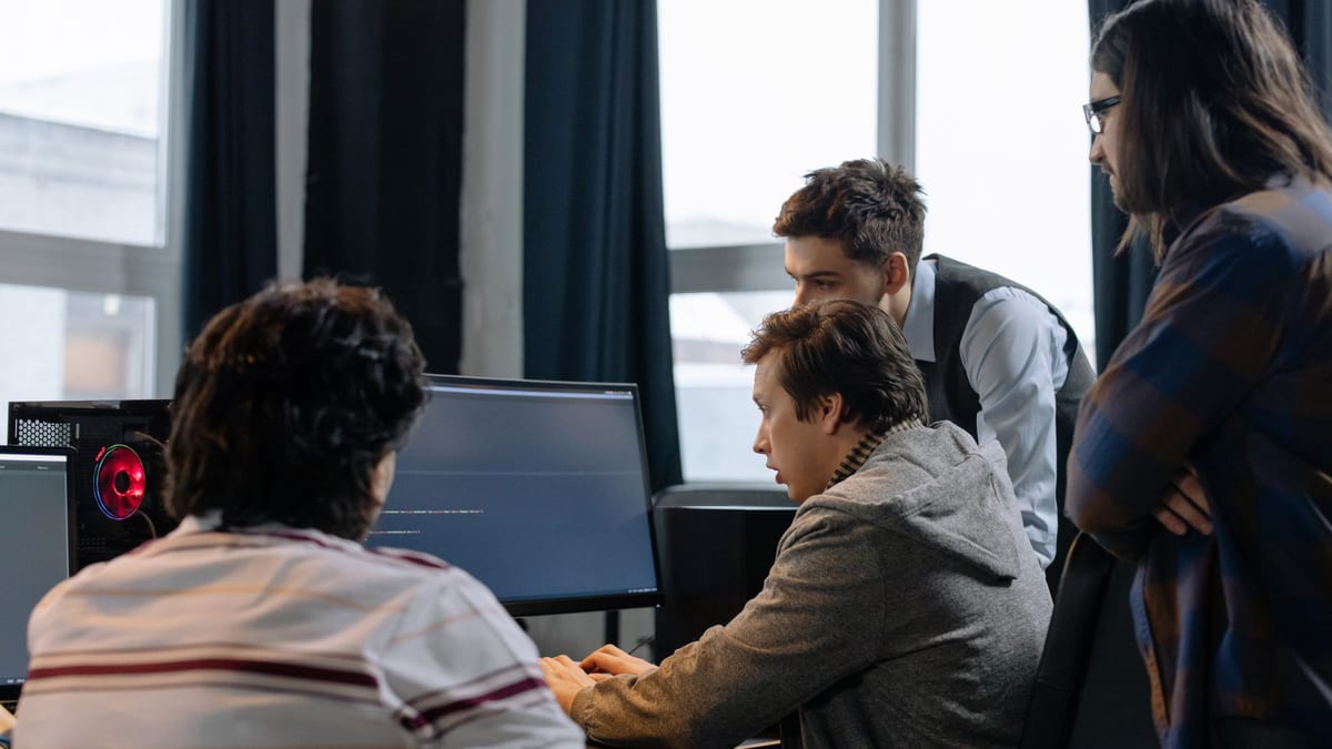 Four colleagues gathered around a monitor showing code, one typing while the others look on