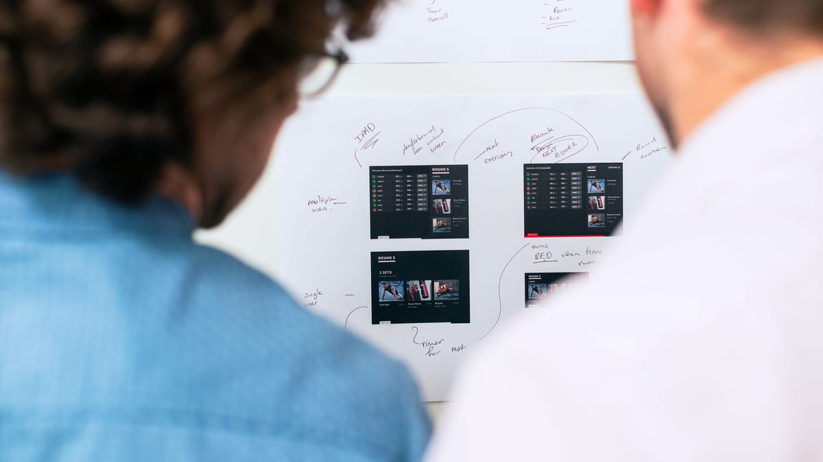 Two colleagues looking at app screen sketches pinned to a whiteboard